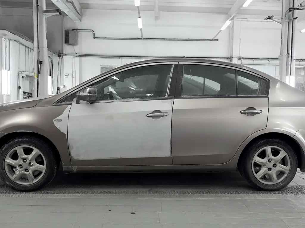 A car in a body shop bay with a repaired door panel.