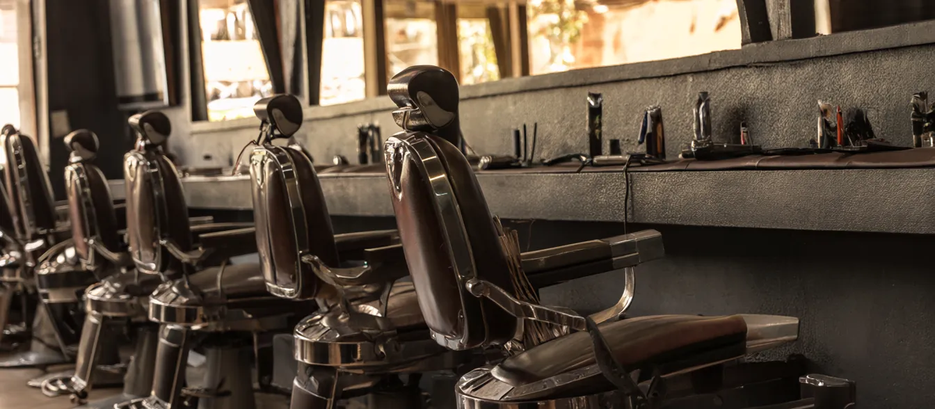 A barber chair beside a long mirror and a shelf of clippers and combs.