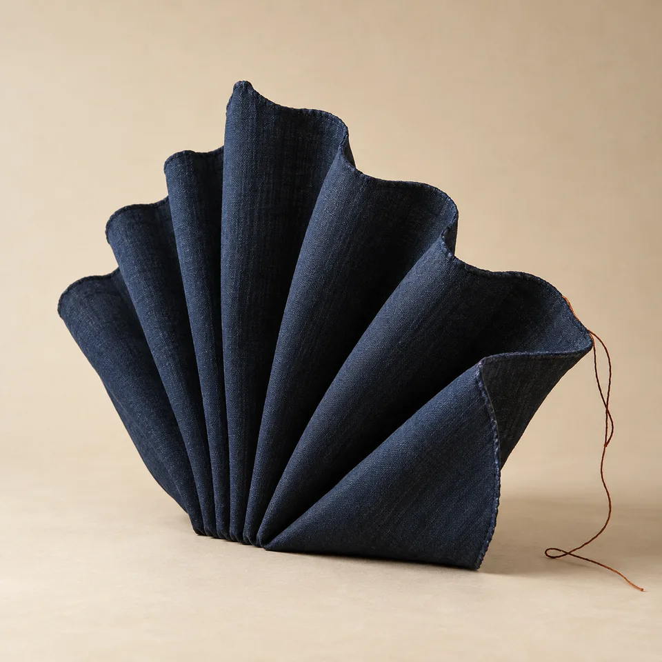 Complete dark indigo pleated textile form with a loose rust thread