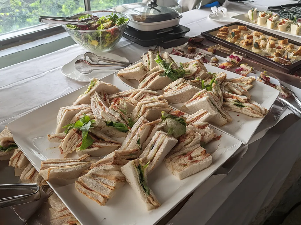 A buffet table with sandwich platters and a salad bowl.