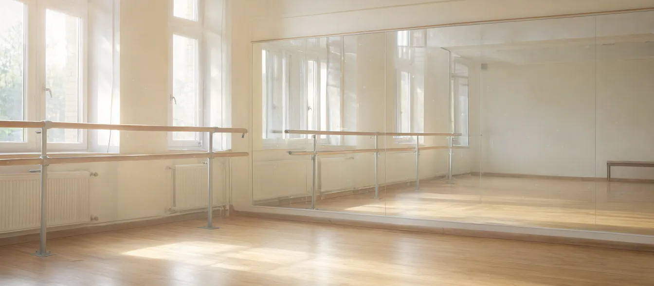 A bright studio with wood floors, a barre along the mirror and tall windows.