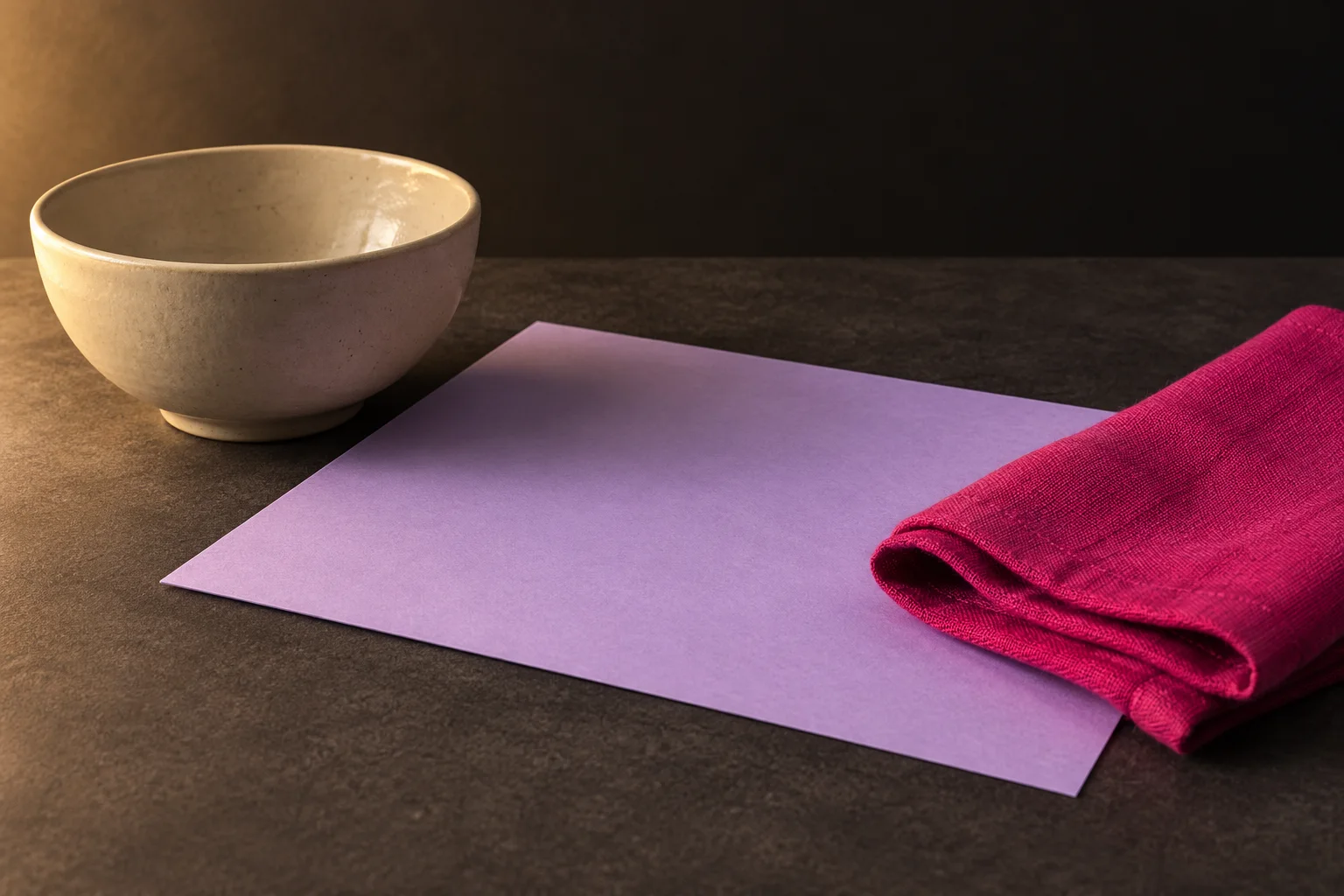 Illustrative evening still life of a ceramic bowl, lavender paper and magenta folded material on a charcoal table