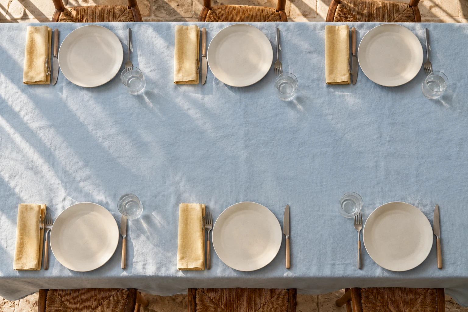 The same pale blue table before arrival, with six place settings and a clear center