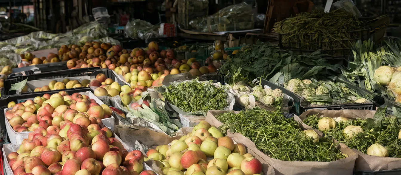 A produce table with apples, leafy greens and bunches of herbs near the entrance.