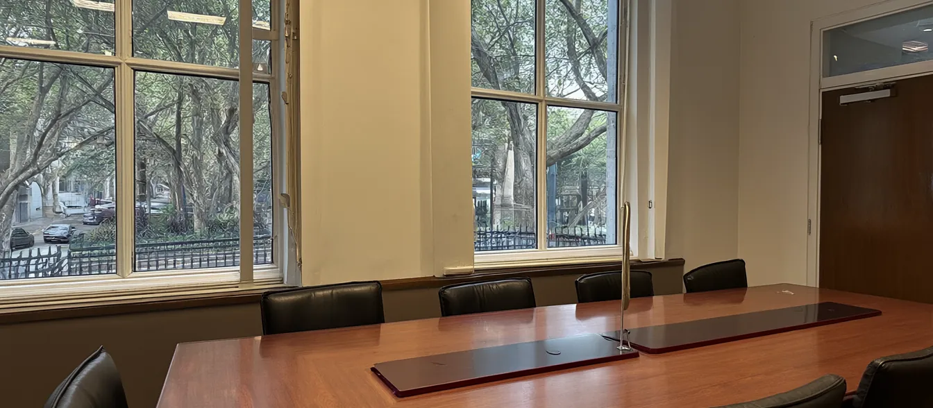 The conference room, with a long wood table and tall windows onto a tree-lined street.