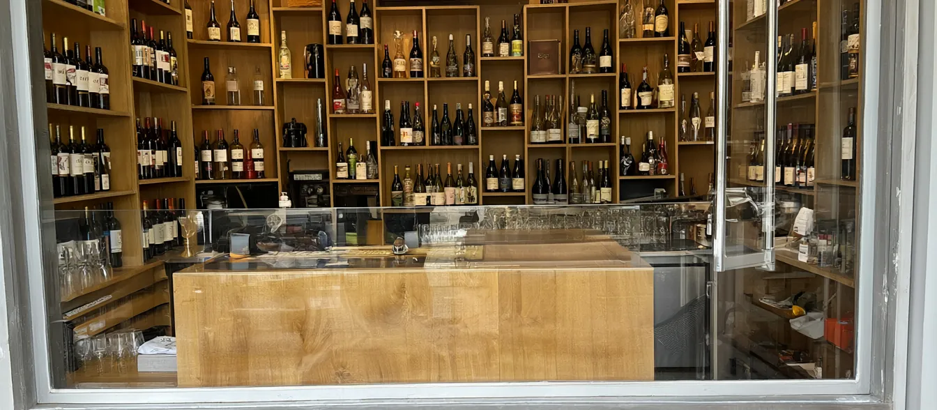 The wine aisle, with bottles on wood shelves and a tasting counter by the front window.
