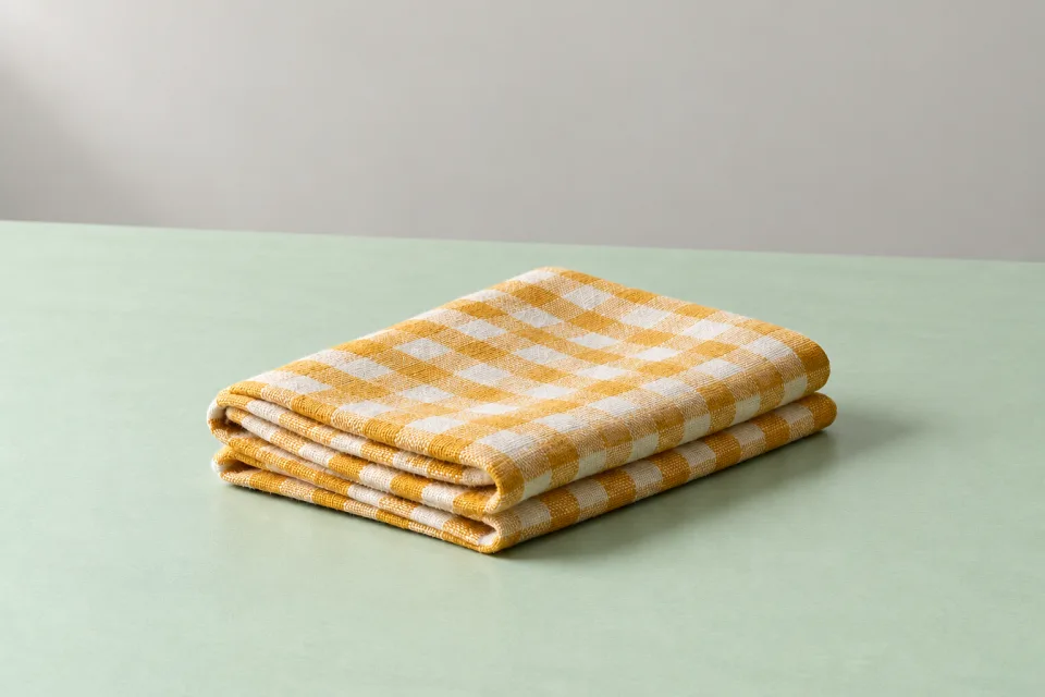 Folded saffron-yellow and ivory small-check cotton-style cloth with visible weave on a mint studio surface