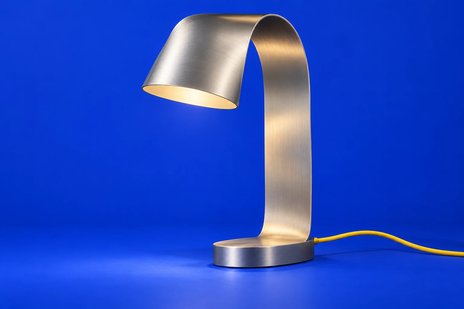 Rill 01, a sculptural ribbon-shaped aluminum lamp with a yellow cable on a cobalt stage.
