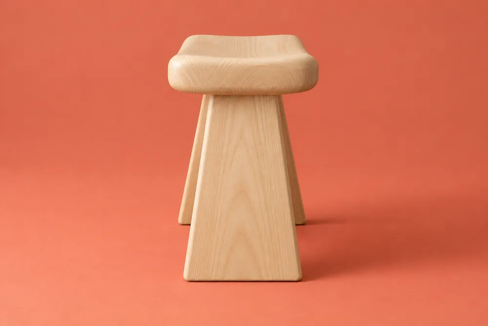 The same illustrative Arc stool viewed from its narrow end, showing the broad slab leg and rounded saddle-seat profile.