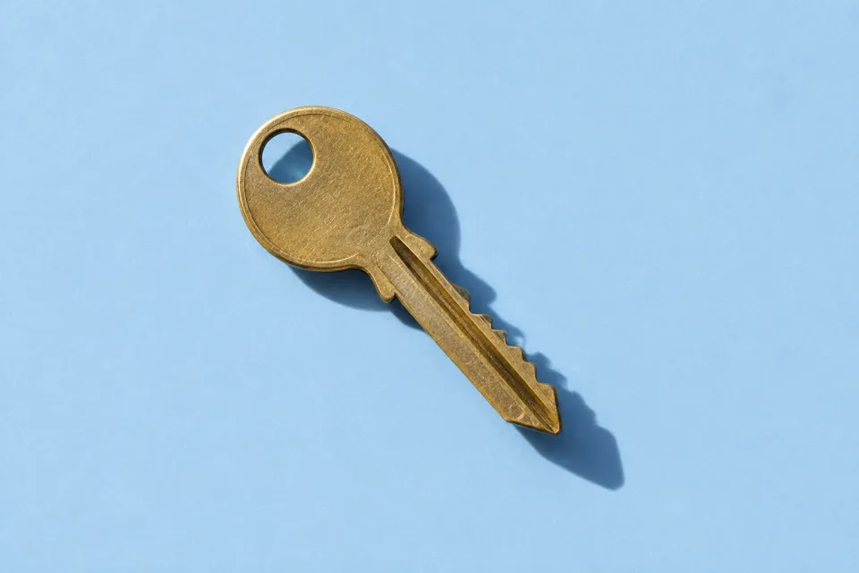 A brass key with an oval bow on pale blue paper, casting a clear diagonal shadow.