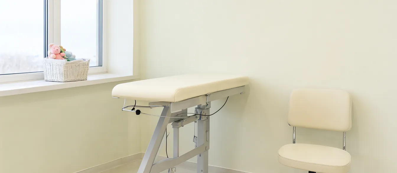 A bright exam room with a child-size chair and a shelf of picture books.