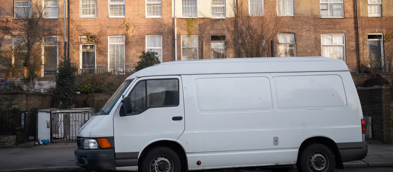 A plain white work van parked in front of a brick townhouse.
