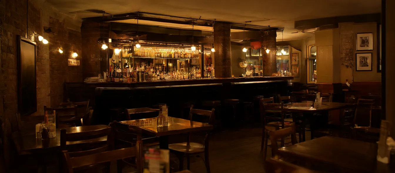 A pub dining room with exposed brick, wooden tables and a long bar.