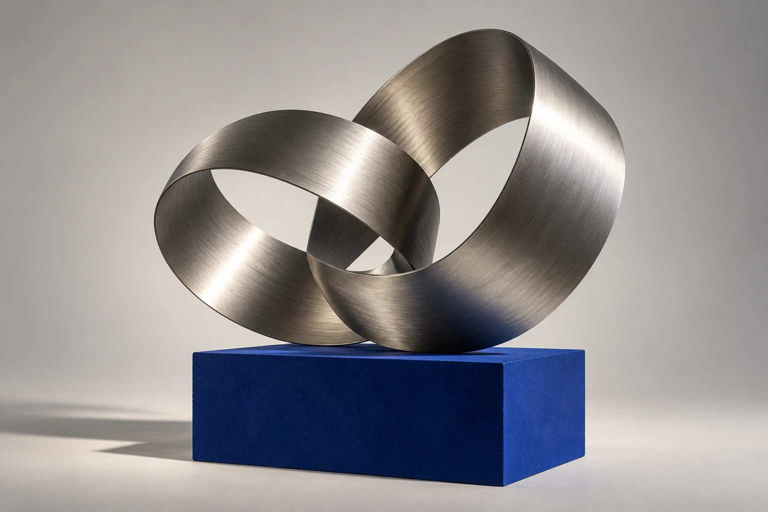 Folded titanium ribbon sculpture balanced on an ultramarine block.