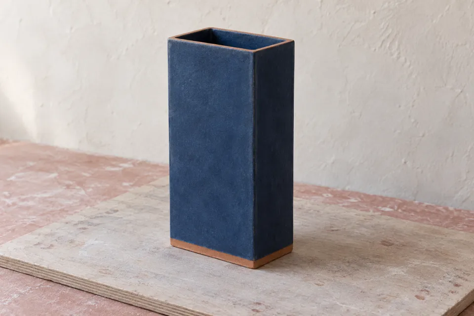 Conceptual finished-surface proposal for the same tall rectangular vessel, matte indigo faces with a narrow terracotta-colored base and thin uncoated rim.