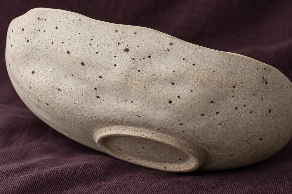 Illustrative underside of the same low vessel family, showing a small recessed oval foot against plum cloth.