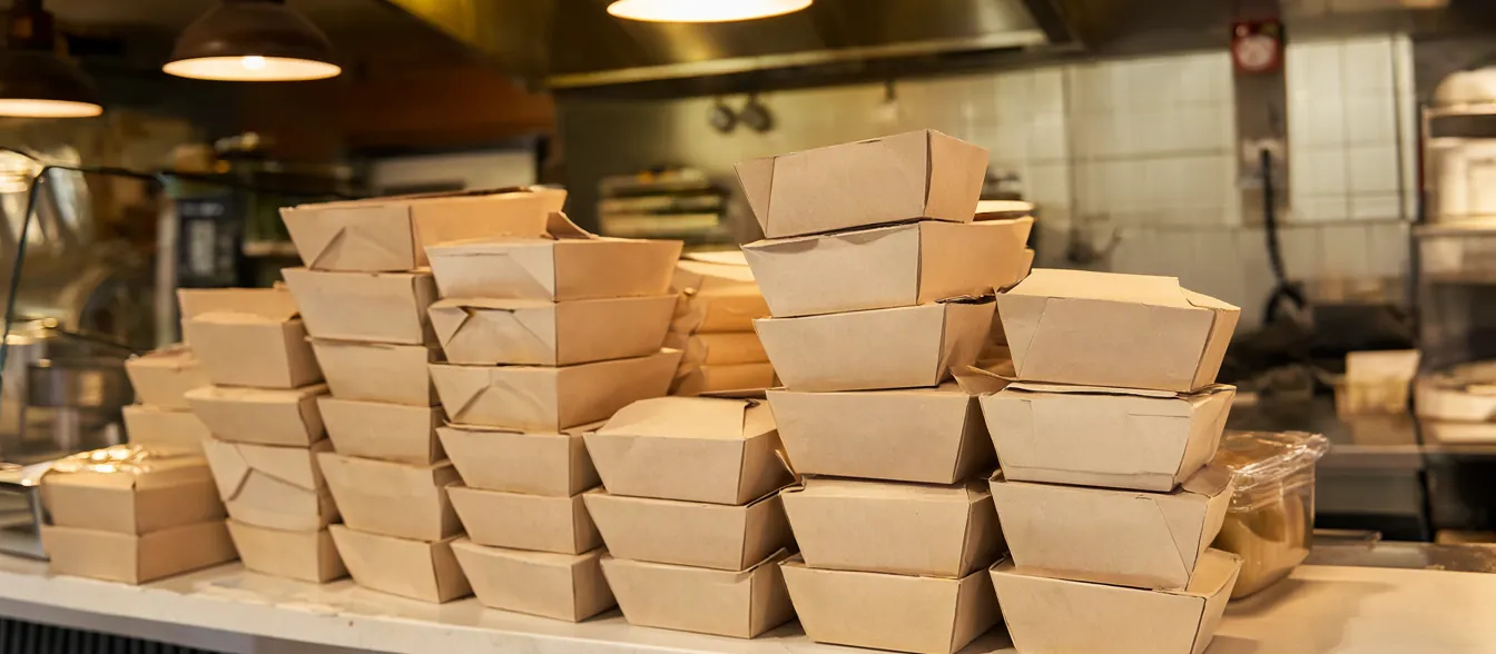 Paper food boxes lined up on a takeout counter beside the kitchen pass.