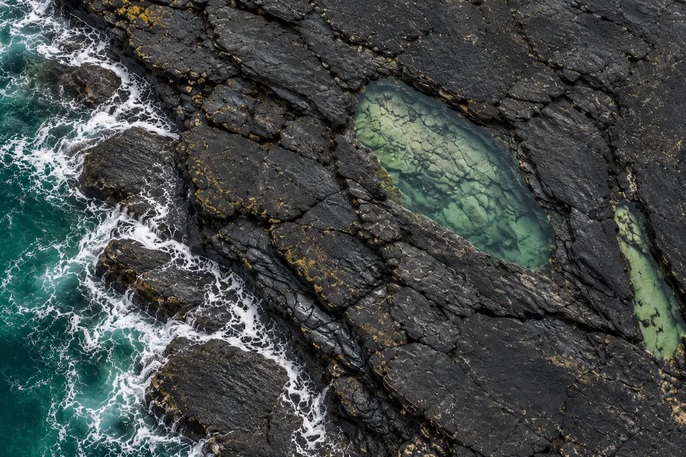 Generated close overhead view of a pale green pool held inside the same dark basalt shelf