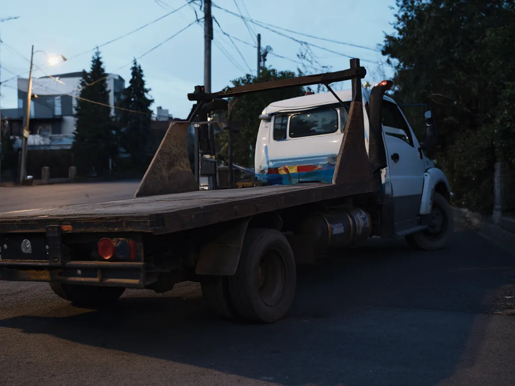 A flatbed tow truck parked on a quiet residential street at dusk.