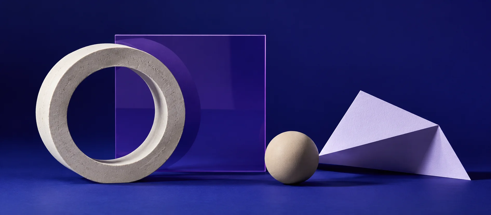 Illustrative studio still life: pale sculptural forms, violet acrylic and folded paper on an indigo field.